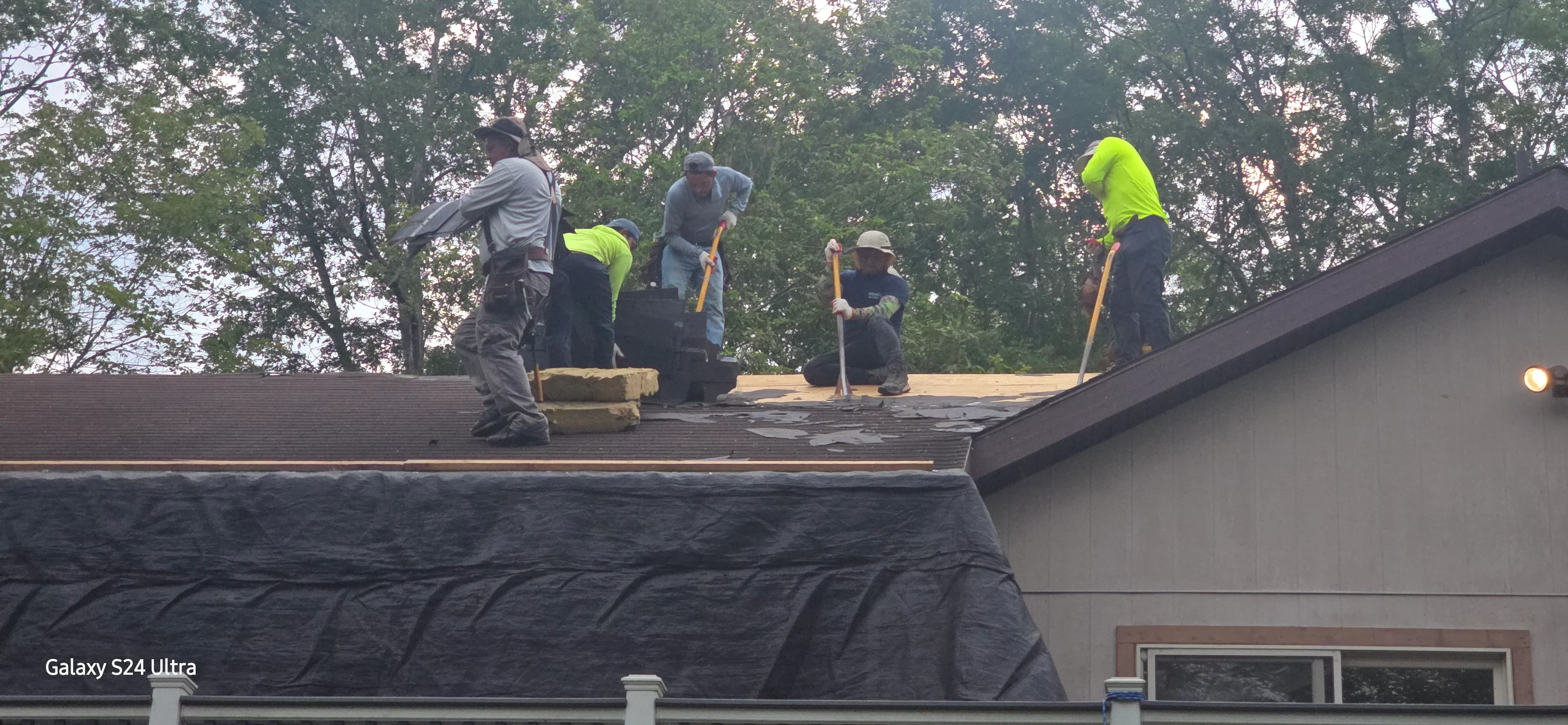 Roofing crew installing asphalt shingles on residential pitched roof with underlayment