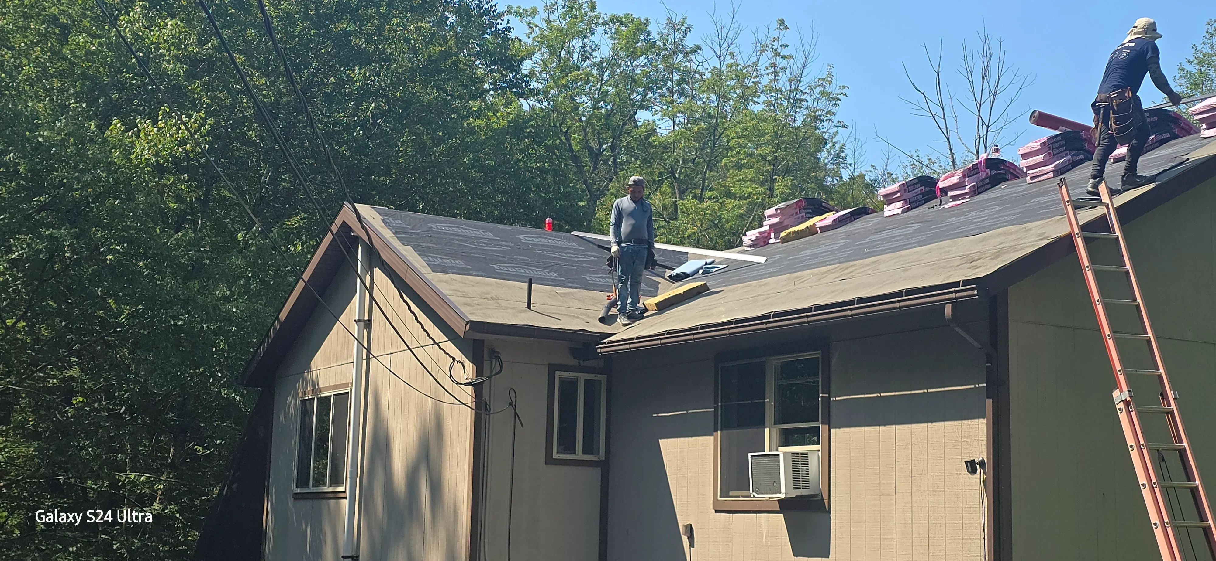 Roofers installing new dark gray asphalt shingles on residential home roof