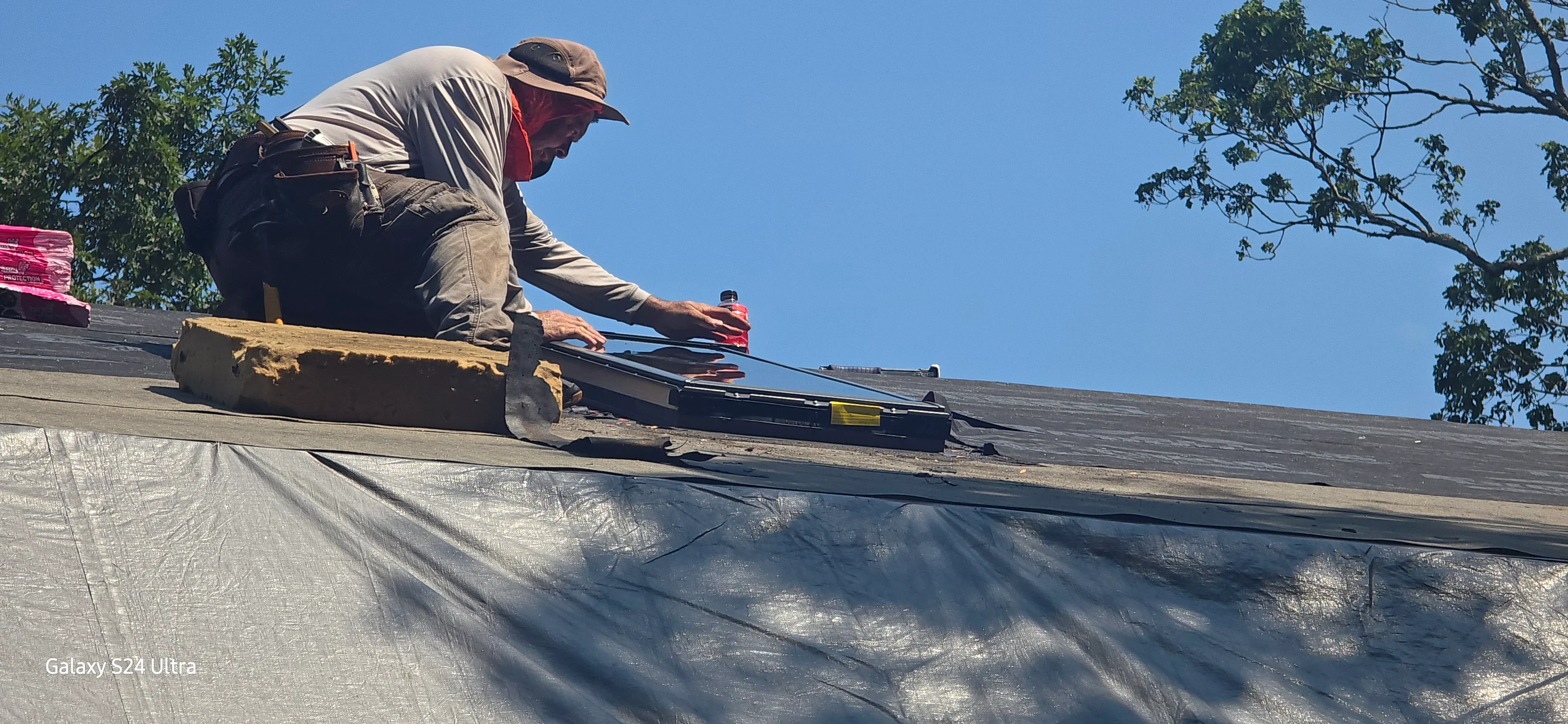 Roofer installing asphalt shingles on residential roof with protective underlayment
