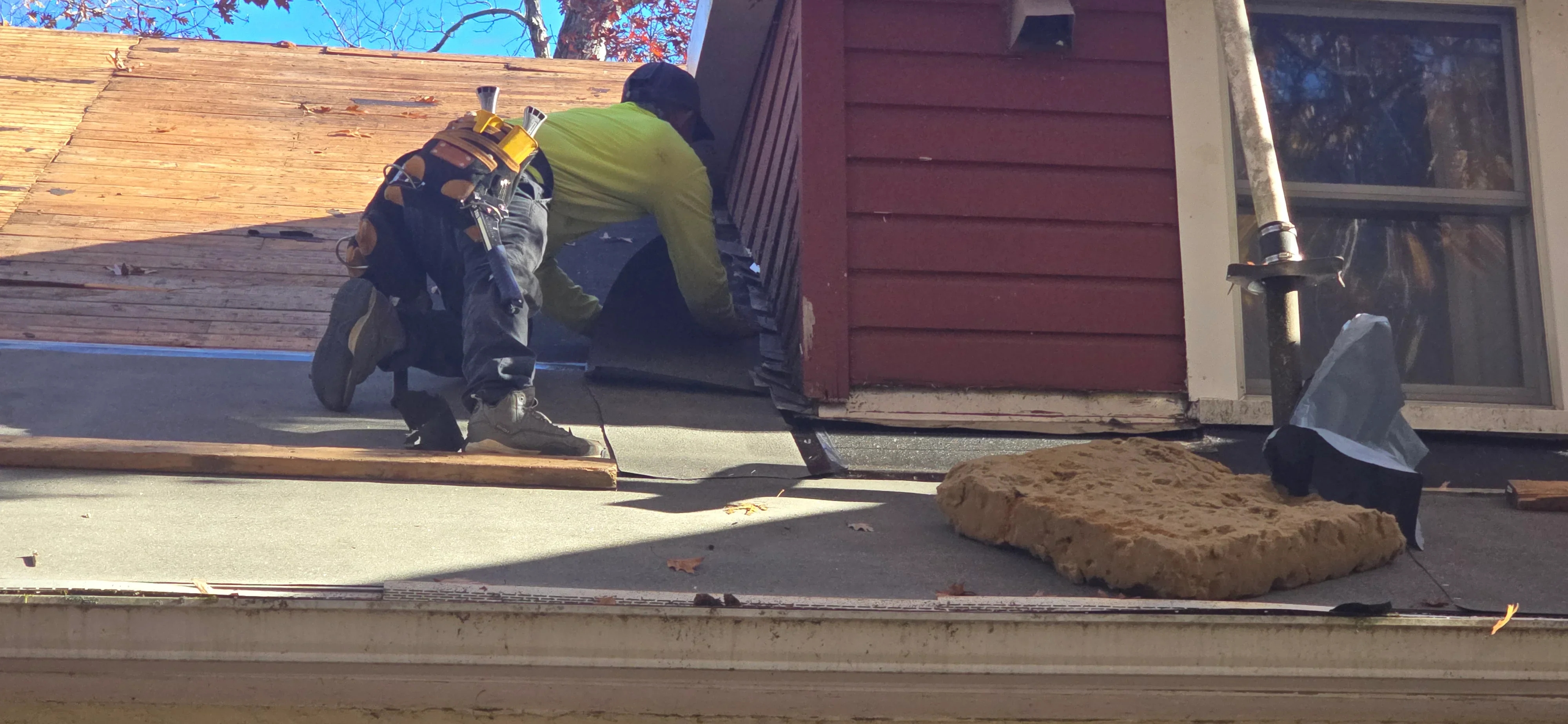 Roofer installing new shingles on residential roof with red garage door visible