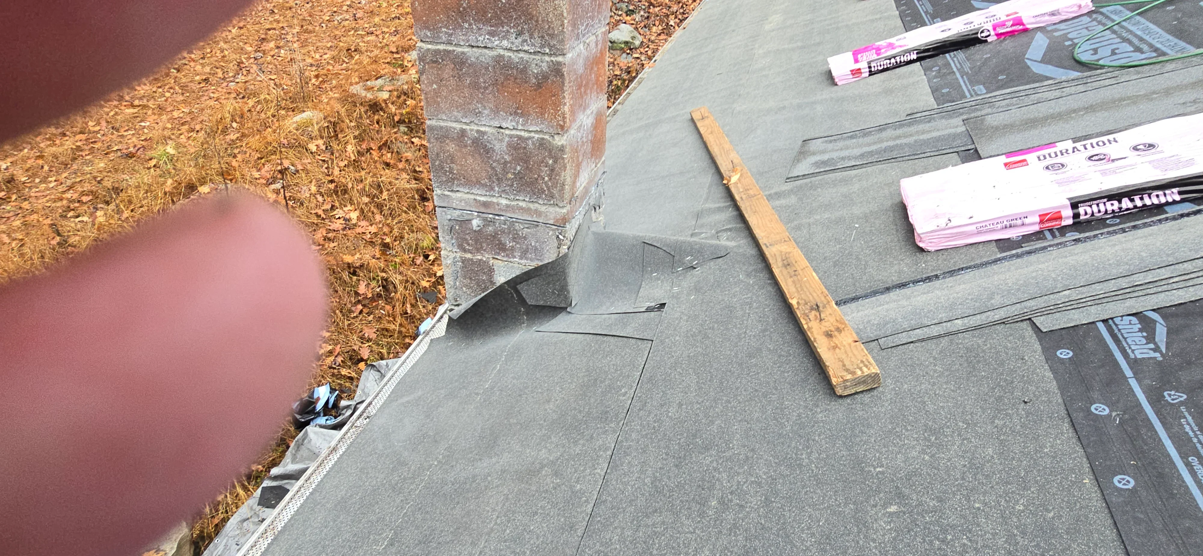 Gray asphalt shingles being installed on roof with underlayment and installation tools visible